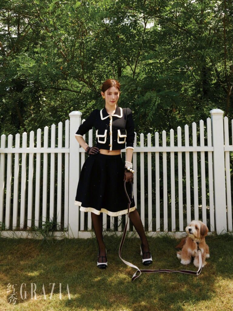 Miyeon in elegant black cropped suit walking her dog by white picket fence in Grazia pictorial