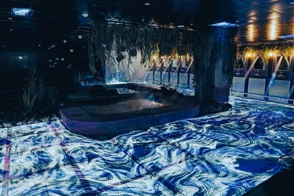 <em>Digital light projections flow across the floor and hot spring pool at Waterworld Jeju, enhancing the futuristic vibe of the <strong>Waterworld Jeju discount</strong> indoor spa experience.</em>