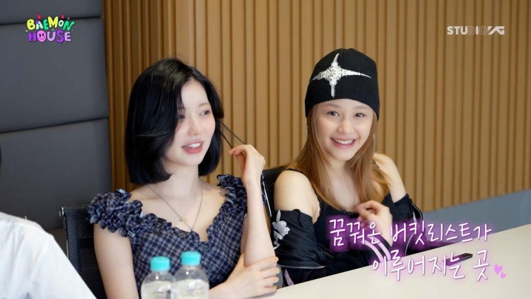BABYMONSTER members Rora and Chikita smiling during a meeting scene in BABYMONSTER reality show