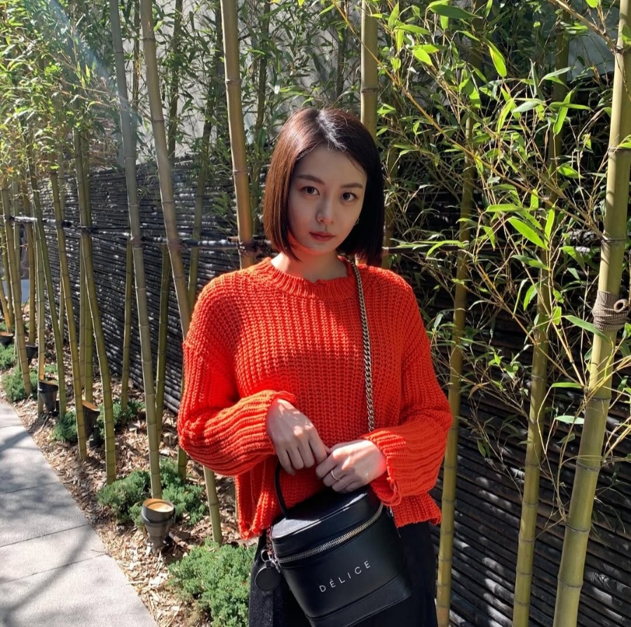 Song Da Eun wears a red sweater outdoors, spotlighted in the Jimin dating scandal.