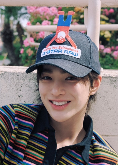 HYBE new boy group CORTIS member in a striped polo shirt and jeans adjusting his cap on a sunny street.