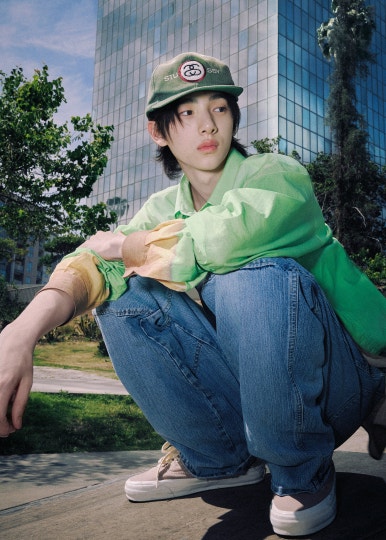 HYBE new boy group CORTIS member in a sleeveless yellow shirt and teal sweatpants standing by a metal railing.