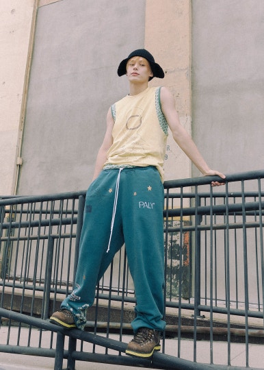 Member of HYBE new boy group CORTIS wearing sunglasses, plaid shirt and sweatpants posing on a city street.