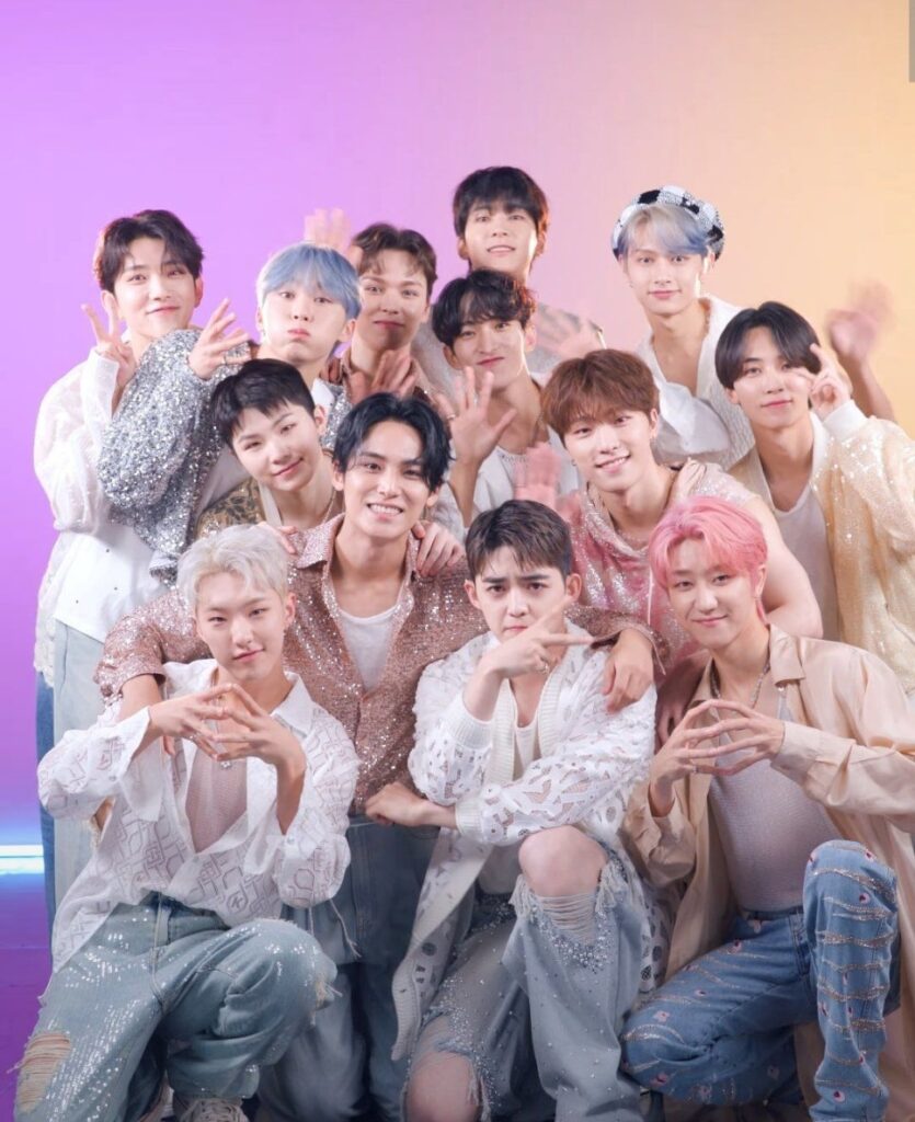 K-pop group Seventeen smiling and posing together in glittering pastel outfits, promoting Seventeen UNESCO donation and global youth support.
