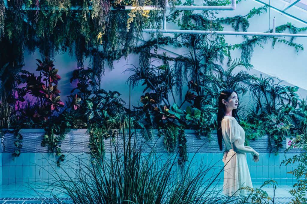 <em>A woman walks through a lush indoor tropical garden with cascading greenery at Waterworld Jeju, a hidden gem offering immersive nature-themed zones and <strong>Waterworld Jeju discount</strong> deals for visitors.</em>