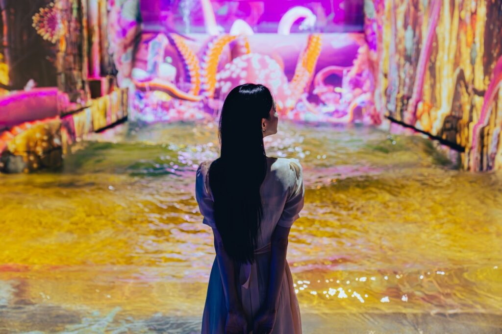 <em>A woman gazes at a giant digital octopus projection inside Waterworld Jeju’s shallow water zone, surrounded by vibrant colors and interactive media art, part of the immersive <strong>Waterworld Jeju discount</strong> experience.</em>