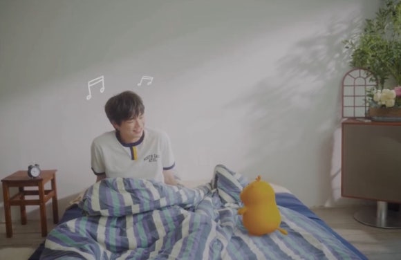 Kang Daniel waking up happily to cartoon character, showing peace despite Los Angeles robbery shock.