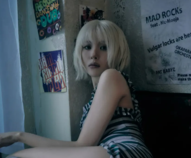 Sunmi leans against a wall of posters in a striped mini dress, capturing a grunge-inspired concept.