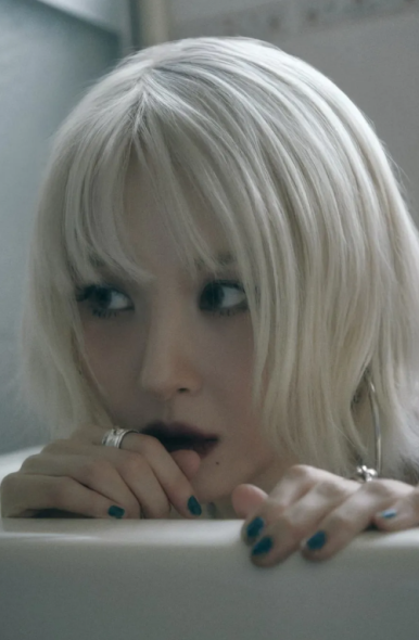 Close-up of Sunmi in a bathtub with smoky makeup and teal nails, expressing intense emotion.