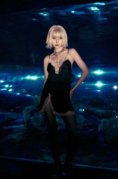 Sunmi poses in front of an aquarium in a black slip dress, channeling a gothic rock vibe.