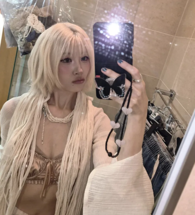 Sunmi takes a mirror selfie in a fringe-knit outfit with platinum blonde hair, revealing her boho-rock style.
