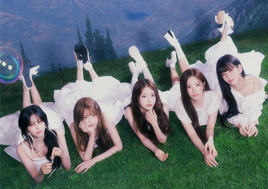 Whimsical group shot for <strong>fromis_9 December comeback</strong> with all members lying on grass, wearing white dresses.