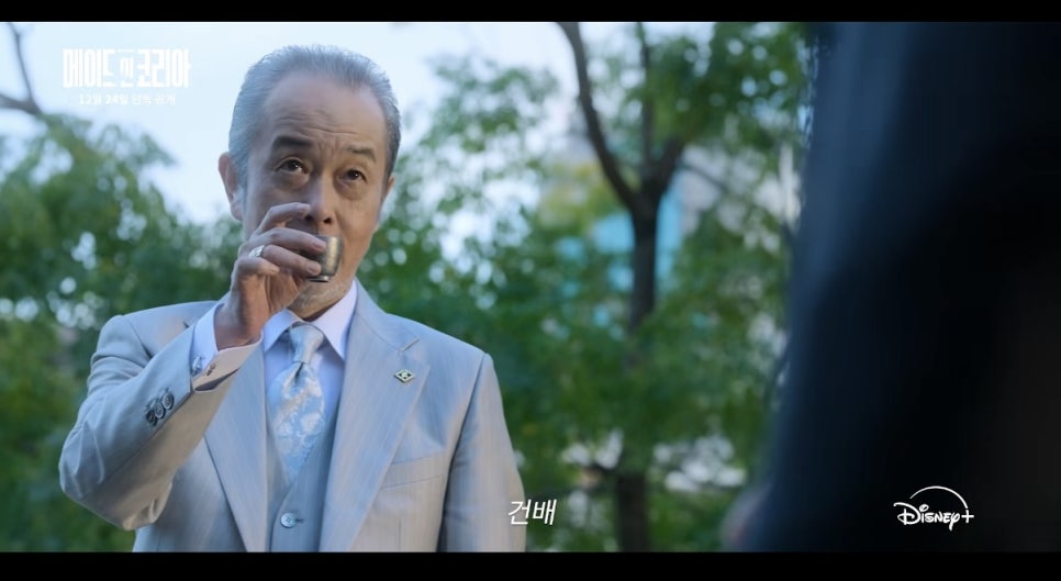 A Japanese official toasts in a tense meeting scene from Made in Korea, symbolizing cross-cultural tension.