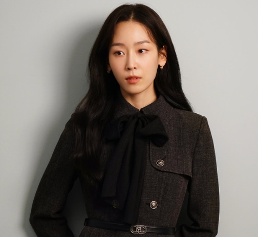 Love Me cast actress in dark gray jacket with ribbon tie, appearing as Jun-kyung’s friend or colleague