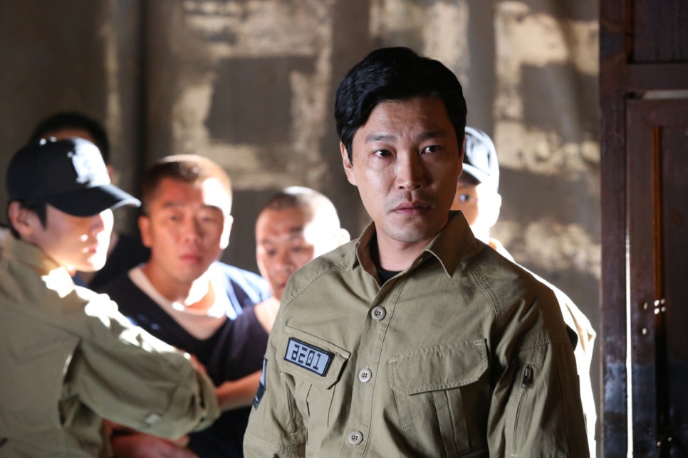 Prison officer overseeing inmates with a serious expression in Fabricated City movie