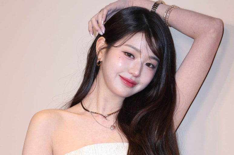 IVE’s Jang Wonyoung posing elegantly in a strapless white dress with hand raised, showcasing luxury accessories
