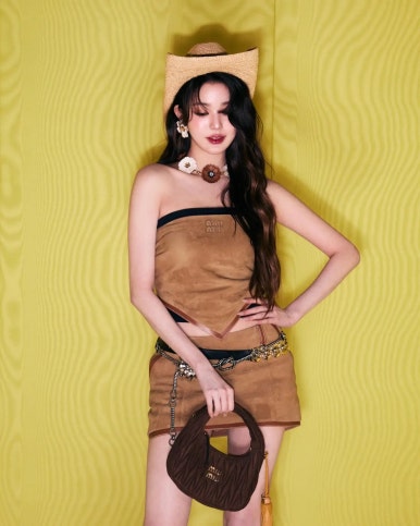 Jang Wonyoung in a cowgirl-inspired brown outfit and mini skirt set, accessorized with a hat and bold jewelry for a fashion campaign