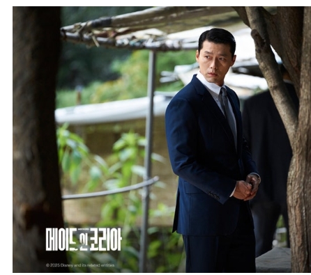 Hyun Bin stands under a tree in Made in Korea, observing his surroundings in a tailored suit.
