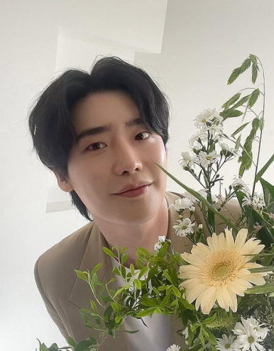 Lee Jong Suk holding spring flowers with a soft smile — image reflecting his gentle aura after fanmeeting cancellation news