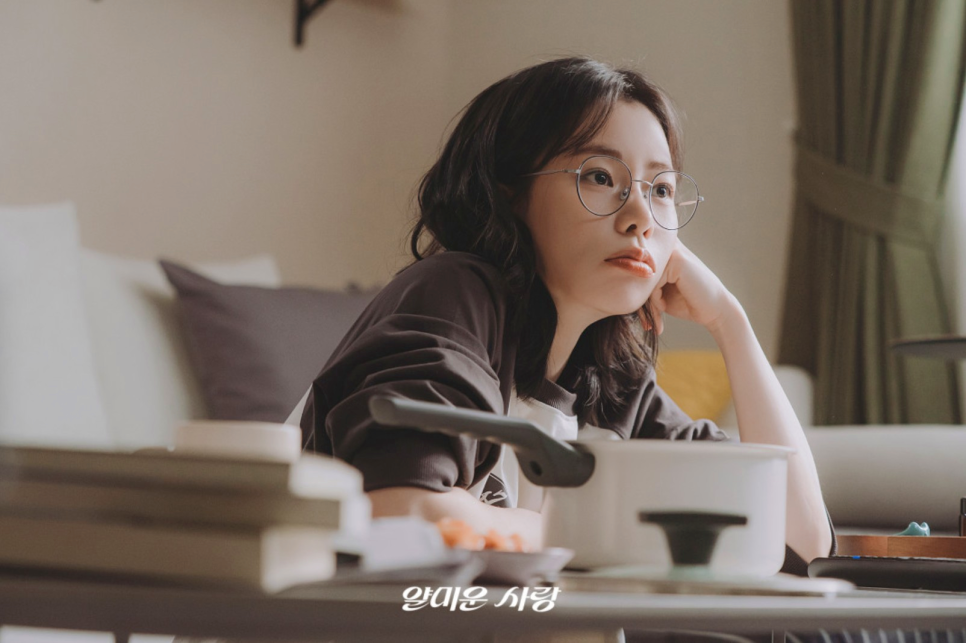 Nice to Not Meet You – A laid-back scene showing the female lead in glasses, reflecting on life in her cozy apartment.